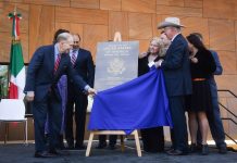 U.S. Ambassador to Mexico Ken Salazar and U.S. Bureau of Overseas Building Operations Director William H. Moser together pull a blue cloth off to reveal a metal plaque bearing the name "Embassy of the United States of America" and the logo of the U.S. Department of State.