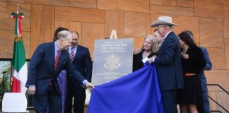 U.S. Ambassador to Mexico Ken Salazar and U.S. Bureau of Overseas Building Operations Director William H. Moser together pull a blue cloth off to reveal a metal plaque bearing the name "Embassy of the United States of America" and the logo of the U.S. Department of State.