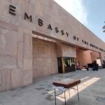 Facade of the new US Embassy in Mexico City. The front of the building is made with pink Mexican cantera stone arranged in rectangles of different sizes and faces a wide courtyard.