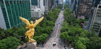 An aerial view of the Angel of Independence monument on Reforma Avenue in Mexico City, looking down the tree-lined boulevard surrounded by tall city buildings.