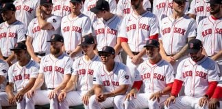 The Boston Red Sox 2024 team sitting on dugout benches in ascending rows for a photo.