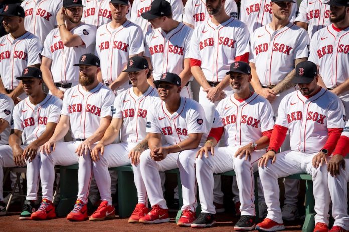 The Boston Red Sox 2024 team sitting on dugout benches in ascending rows for a photo.