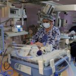 A masked doctor attends to a tiny infant in a hospital incubator