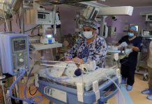 A masked doctor attends to a tiny infant in a hospital incubator