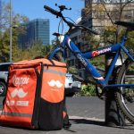 A blue mountain bike with a Rappi food delivery backpack case, both chained to a post in Mexico City.