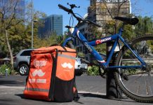 A blue mountain bike with a Rappi food delivery backpack case, both chained to a post in Mexico City.