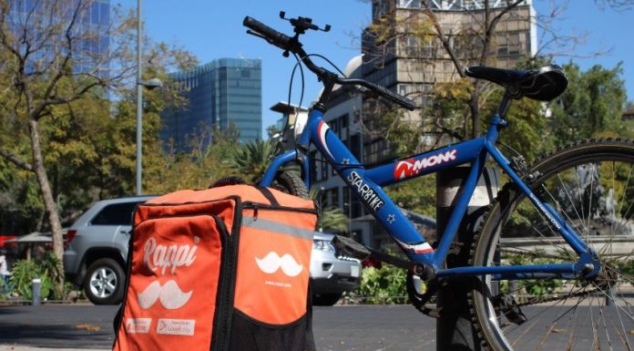 A blue mountain bike with a Rappi food delivery backpack case, both chained to a post in Mexico City.