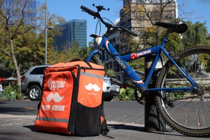 A blue mountain bike with a Rappi food delivery backpack case, both chained to a post in Mexico City.