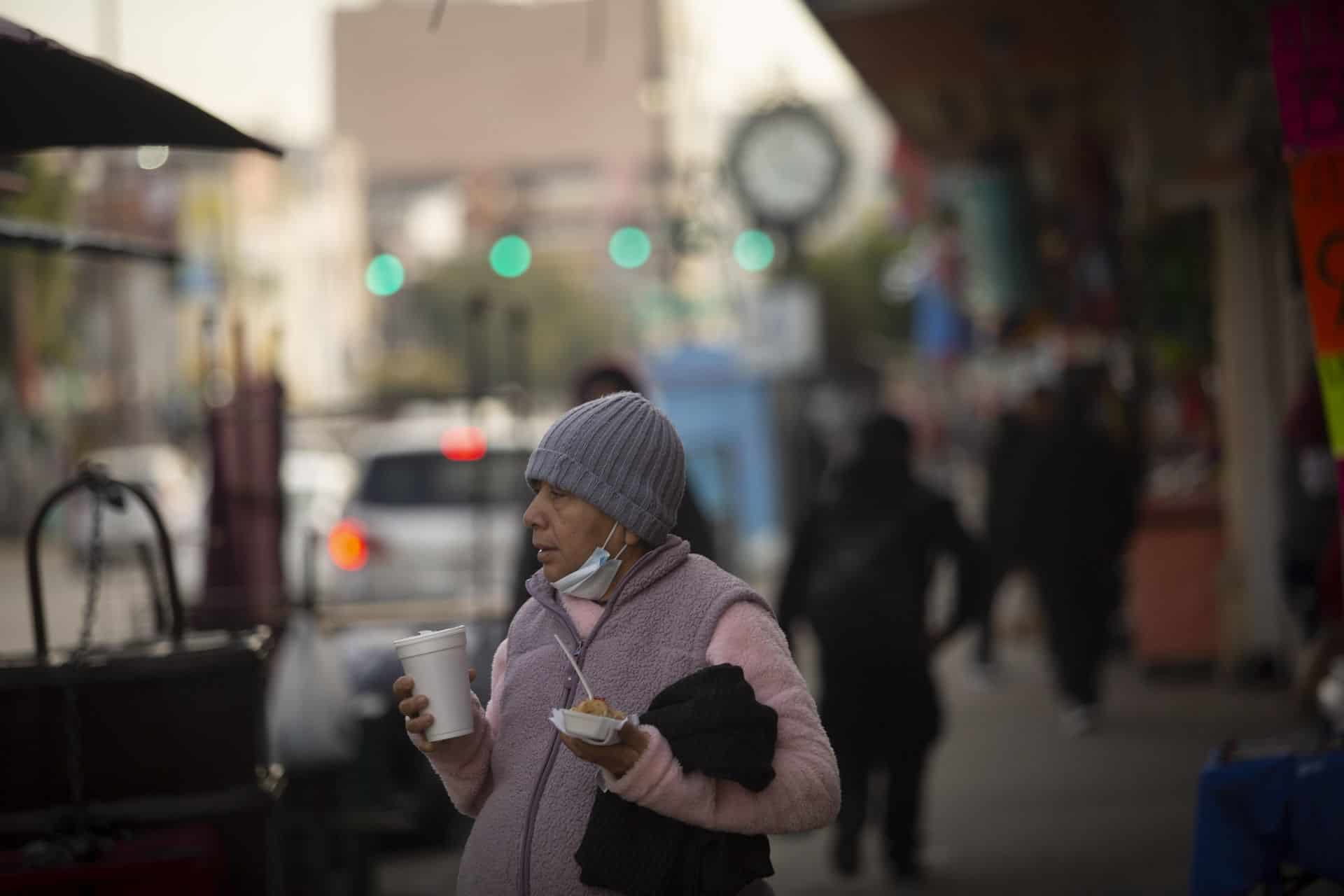 Woman with tamale and champurrado in the downtown area of ​​Tijuana sheltered from the low temperatures.