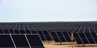 Thousands of solar panels in rows at an angle facing up at the sky in a desert area of Sonor