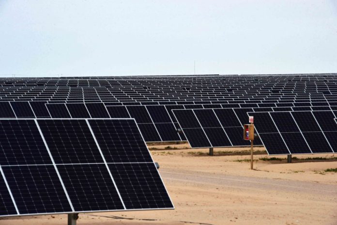 Thousands of solar panels in rows at an angle facing up at the sky in a desert area of Sonor