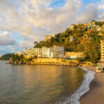 Coastal view of a sandy beach with resorts and hillside homes in Puerto Vallarta, Mexico.