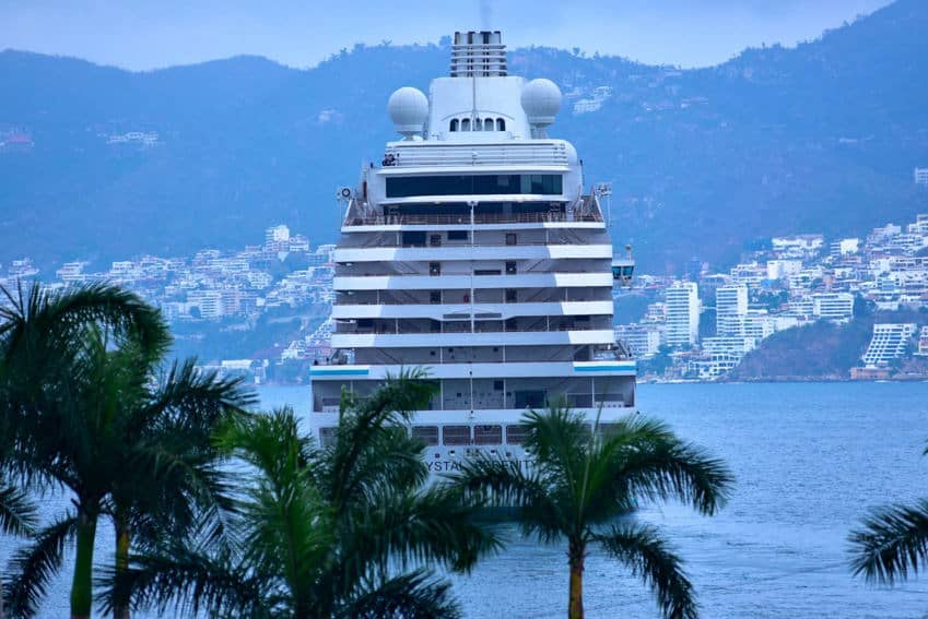 The back of a cruise ship docked in the port of Acapulco with the city and Acapulco's mountainous skyline in the distance.