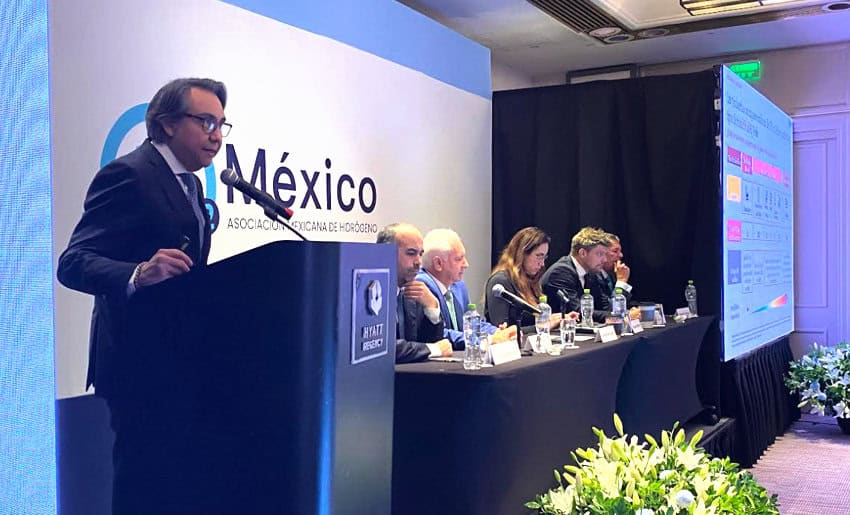 Mexican green hydrogen lobbyist Israel Hurtado speaking at a press conference podium at a hotel in Mexico City, while a panel of experts listen on at a banquet table to his left.