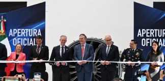Mexican-government and Safran officials in a horizontal line preparing to cut a ribbon launching a new assembly line at Safran's aerospace parts manufacturing plant.