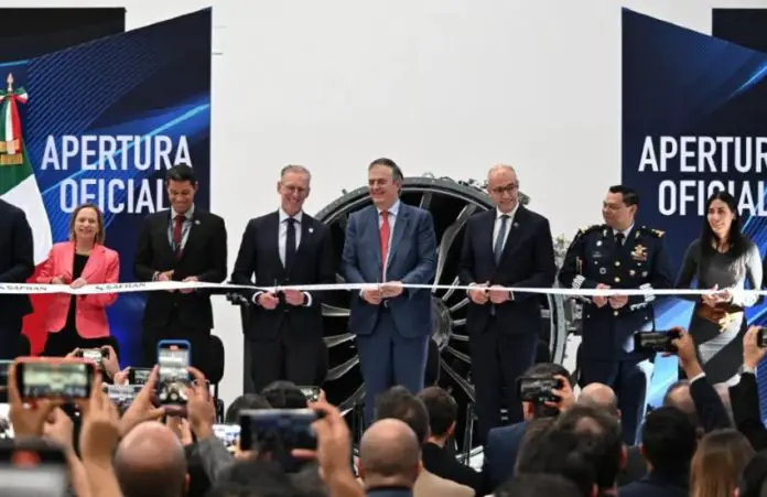 Mexican-government and Safran officials in a horizontal line preparing to cut a ribbon launching a new assembly line at Safran's aerospace parts manufacturing plant.