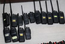 Black two way communication radios with labels on each bearing a different number written in marker, lying on a table on display.