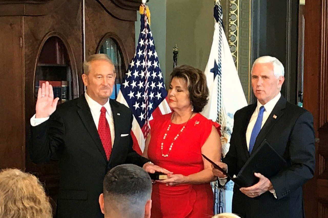 Ronald Johnson, left, holding up his right hand before him and his left on a book held by a woman next to him as Johnson is sworn in as U.S. ambassador to El Salvador. Former Vice President Mike Pence is at the far right, holding an open black portfolio folder.