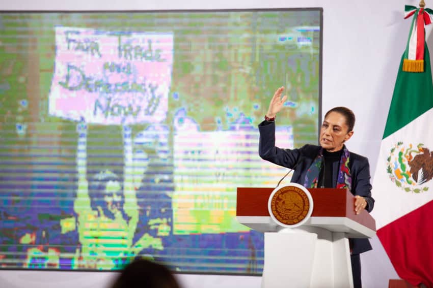 Mexico's President Claudia Sheinbaum speaking to reporters at her press conference while behind her on a projection screen is a photo of her in 1991 protesting at California's Stanford University