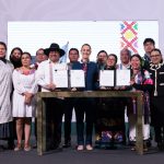 President Claudia Sheinbaum, center, poses with smiling government officials and Indigenous community representatives as they hold up two official presidential decrees for the camera.