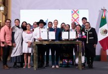 President Claudia Sheinbaum, center, poses with smiling government officials and Indigenous community representatives as they hold up two official presidential decrees for the camera.