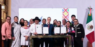 President Claudia Sheinbaum, center, poses with smiling government officials and Indigenous community representatives as they hold up two official presidential decrees for the camera.
