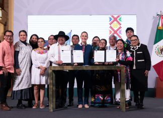 President Claudia Sheinbaum, center, poses with smiling government officials and Indigenous community representatives as they hold up two official presidential decrees for the camera.