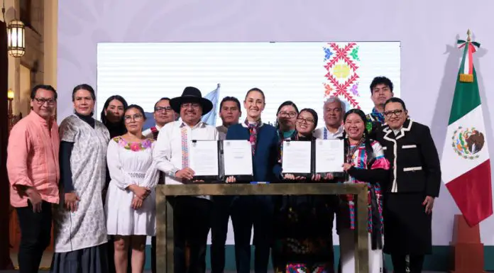 President Claudia Sheinbaum, center, poses with smiling government officials and Indigenous community representatives as they hold up two official presidential decrees for the camera.