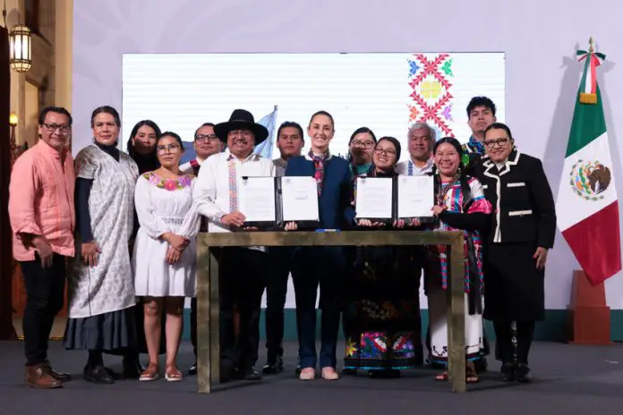 President Claudia Sheinbaum, center, poses with smiling government officials and Indigenous community representatives as they hold up two official presidential decrees for the camera.