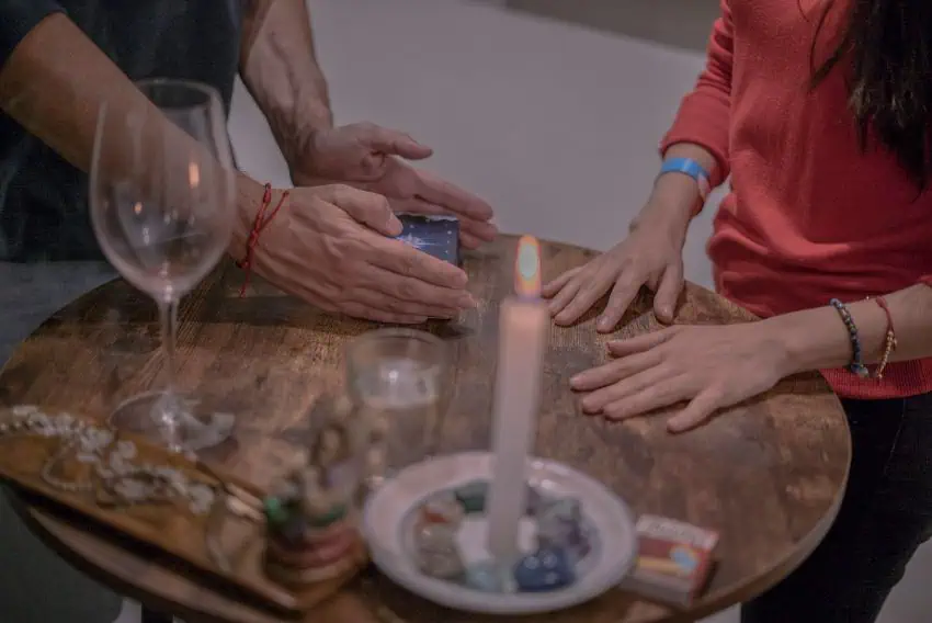 Tabletop with two pairs of hands, mystic objects, wine glass and candle