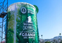 A massive 'Margarita Cachanilla' statue in Tijuana, Mexico. resembling an oversized cocktail cup, with the words "Guinness World Records Official Attempt" visible, promoting "La Margarita Más Grande del Mundo' (The World's Largest Margarita). The structure stands under a clear blue sky with the Tijuana skyline in the background.