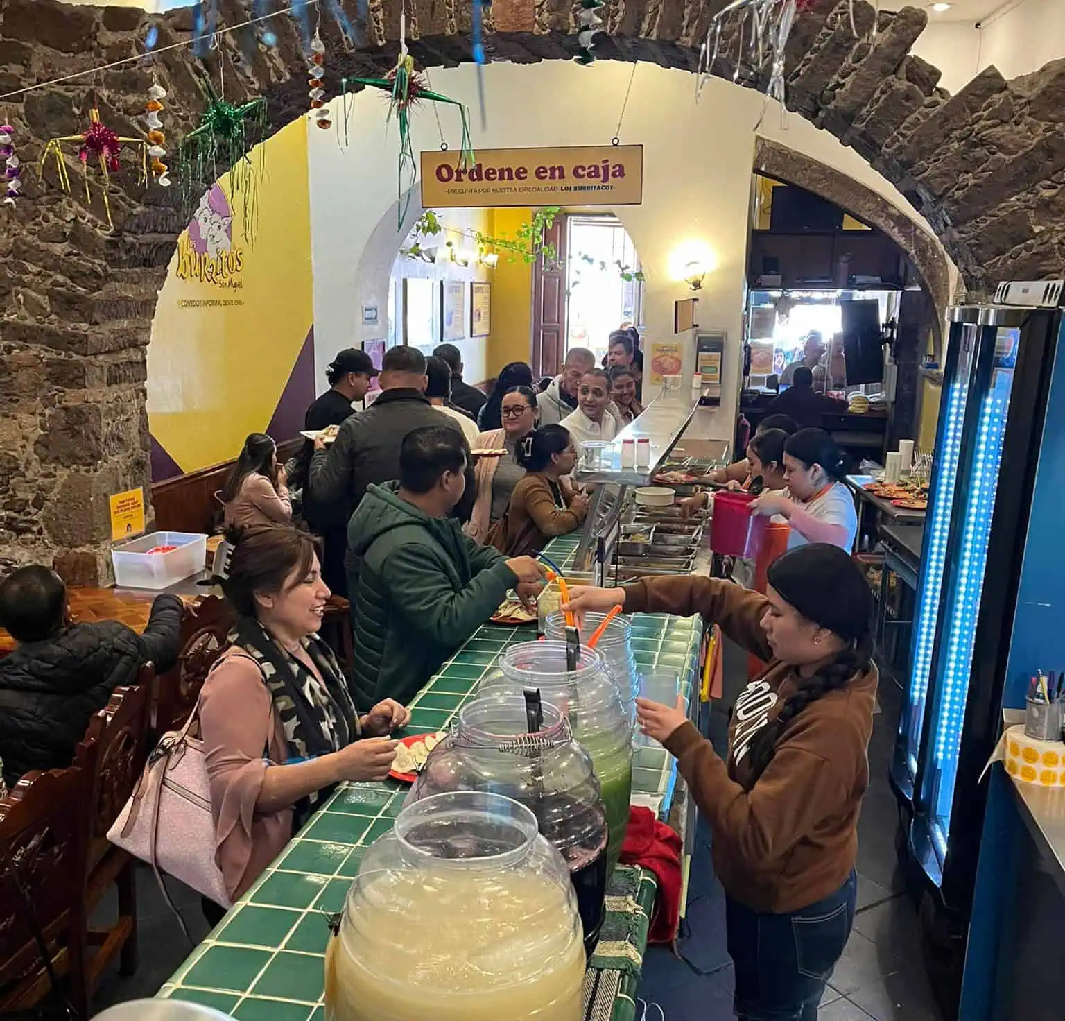 Cooks serve drinks and food to customers in a Mexican restaurant