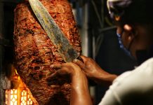 A taquero cuts meat of a trombo of al pastor taco meat.