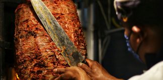 A taquero cuts meat of a trombo of al pastor taco meat.