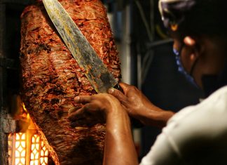 A taquero cuts meat of a trombo of al pastor taco meat.