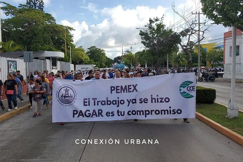 Protesters march down a street holding a banner reading "Pemex: el trabajo ya se hizo, Pagar es su compromiso"