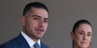 Security Minister García Harfuch speaks at a microphone while Presiden Sheinbaum stands nearby