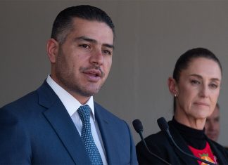 Security Minister García Harfuch speaks at a microphone while Presiden Sheinbaum stands nearby