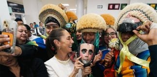 President Sheinbaum laughs surrounded by supporters in traditional Chiapas clothing, while holding a ceremonial mask
