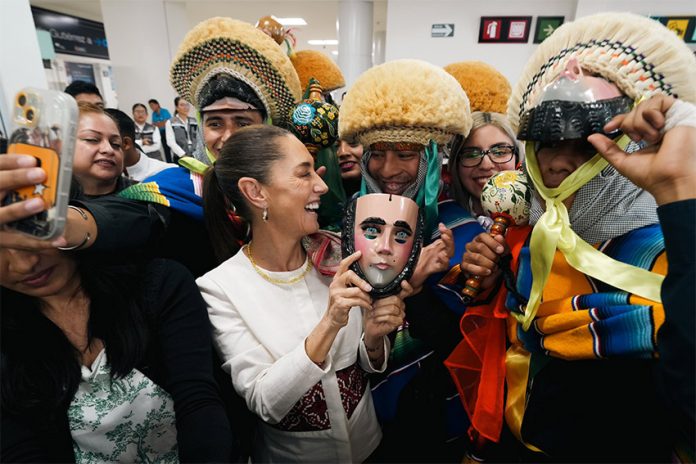 President Sheinbaum laughs surrounded by supporters in traditional Chiapas clothing, while holding a ceremonial mask