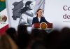 President Claudia Sheinbaum stands at a podium next to a Mexican flag at her morning press briefing