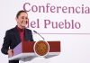 Mexican President Claudia Sheinbaum stands smiling at a podium in front of the words "Conferencia del Pueblo"