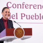 Mexican President Claudia Sheinbaum stands smiling at a podium in front of the words "Conferencia del Pueblo"