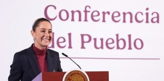 Mexican President Claudia Sheinbaum stands smiling at a podium in front of the words "Conferencia del Pueblo"