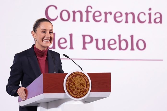 Mexican President Claudia Sheinbaum stands smiling at a podium in front of the words 