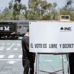 A Mexican voter fills out a ballot in a voting booth bearing the words "INE" and "El voto es libre y secreto."