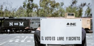 A Mexican voter fills out a ballot in a voting booth bearing the words "INE" and "El voto es libre y secreto."