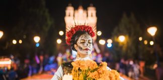 Mexican woman dressed as a Catrina and in white skeletal makeup holding Mexican marigolds