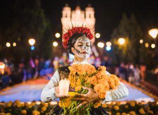 Mexican woman dressed as a Catrina and in white skeletal makeup holding Mexican marigolds