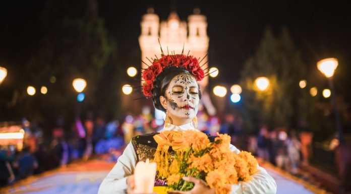 Mexican woman dressed as a Catrina and in white skeletal makeup holding Mexican marigolds